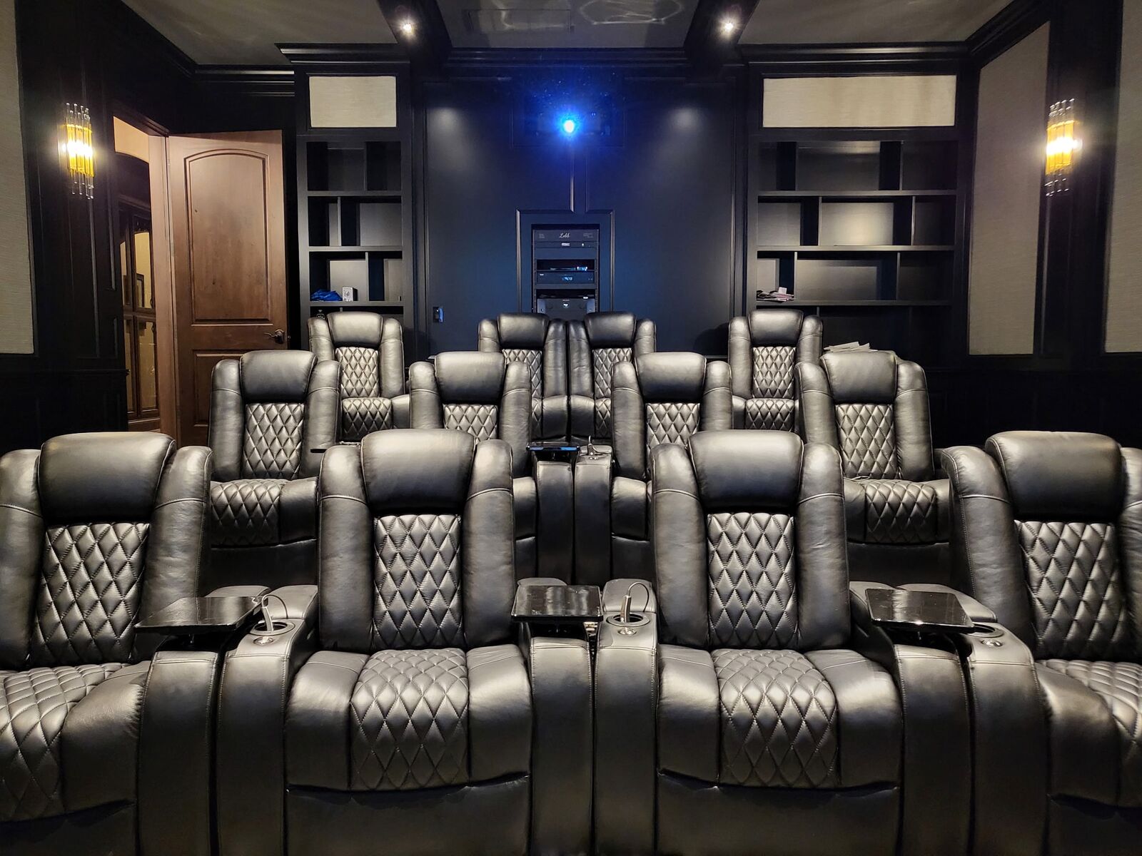 Three tiers of black leather theater recliners in a dark theater